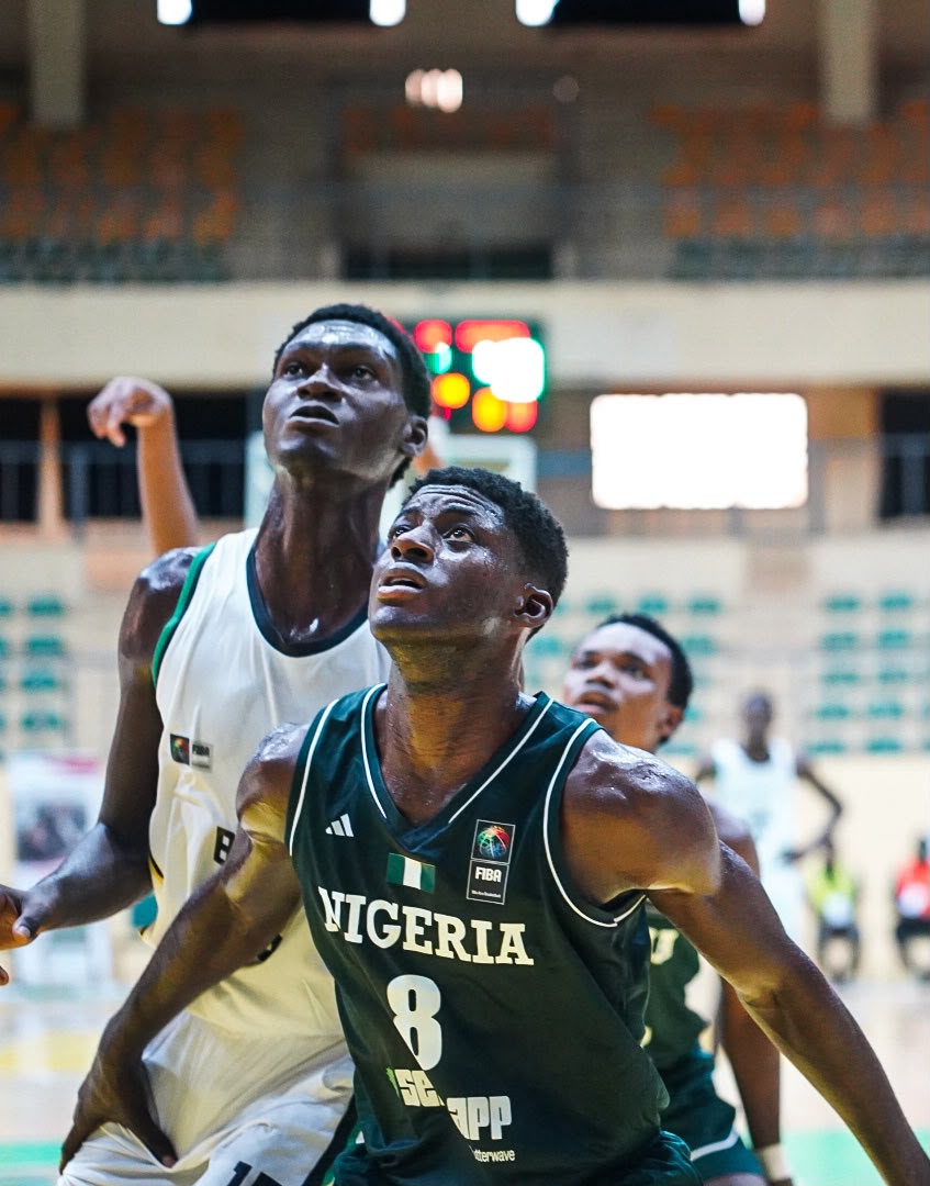 Two basketball players under a hoop fight for position Nigeria jersey number 8 in green foreground defender in white behind indoors arena with blurred scoreboard in background  trybalnews