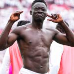 Muscular shirtless man posing with arms raised at a stadium crowd blurred in the background celebrating  trybalnews