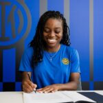 Smiling woman in a blue shirt signs documents at a white desk wearing an Inter Milan badge on her chest  trybalnews