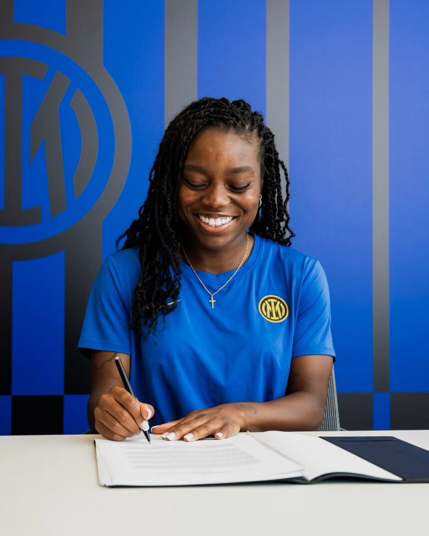 Smiling woman in a blue shirt signs documents at a white desk wearing an Inter Milan badge on her chest  trybalnews