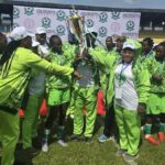 Women soccer team in neon green uniforms lifting a gold trophy on a grassy field  trybalnews