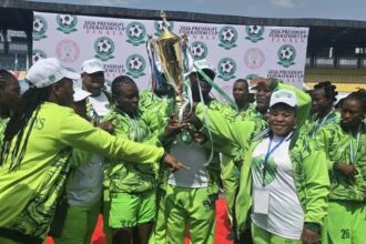 Women soccer team in neon green uniforms lifting a gold trophy on a grassy field.