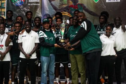 Group of Nigerian basketball players and staff posing with a trophy after a win ceremony.