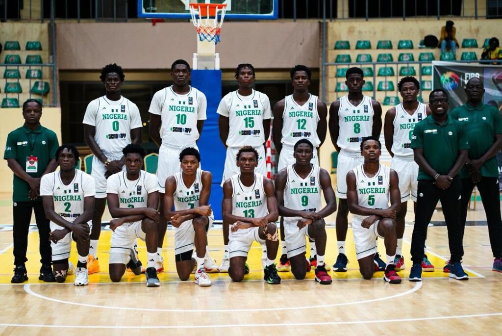Nigerias U18 boys national team Trybal News Group photo of Nigeria basketball team on a court players in white uniforms with green numbers kneeling and standing in front of a hoop trybalnews