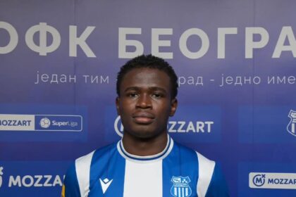 Young male soccer player in a blue-and-white striped jersey posing for a photo with a blue sponsor backdrop showing Mozzart logos and a team crest on his chest.