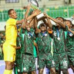 Soccer team in green and black celebrate holding a large silver trophy aloft confetti flying  trybalnews
