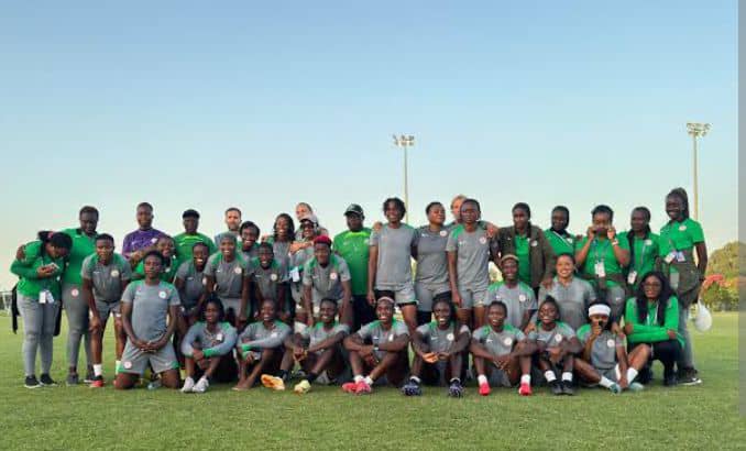 Group photo of a soccer team wearing gray and green uniforms posing on a grass field with coaches standing at the back under a clear sky  trybalnews
