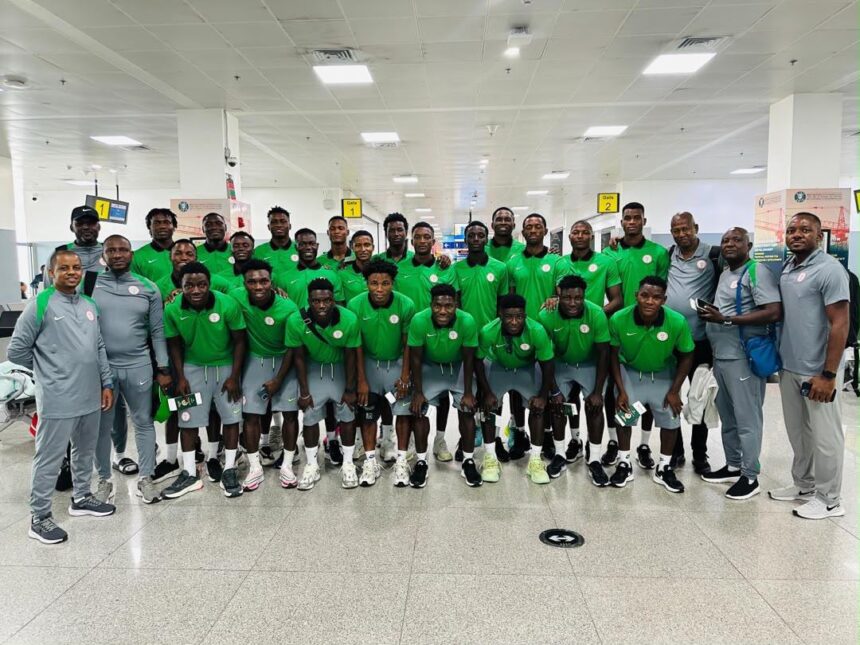 Large group of male athletes in matching green jerseys and gray shorts pose for a team photo in a bright airport terminal with several coaches in gray nearby  trybalnews