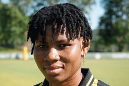 Portrait of a person with short dreadlocks wearing a black-and-yellow striped soccer jersey outdoors.