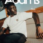 Promotional poster showing a man seated inside a boat with cushioned seating he wears a white T shirt dark pants and a wristwatch Large white text across the top reads Adams smaller text states 26 yo  Nigeria  Forward A small badge is on the shirt  trybalnews