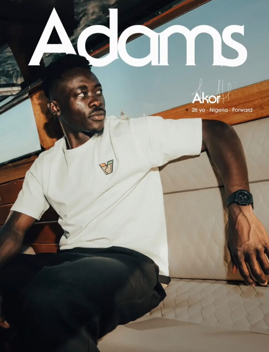 Promotional poster showing a man seated inside a boat with cushioned seating he wears a white T shirt dark pants and a wristwatch Large white text across the top reads Adams smaller text states 26 yo  Nigeria  Forward A small badge is on the shirt  trybalnews
