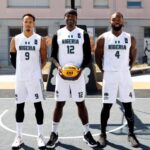 Three Nigerian basketball players posing on an outdoor court in white jerseys numbers 9 12 and 4 with the center player holding a basketball  trybalnews