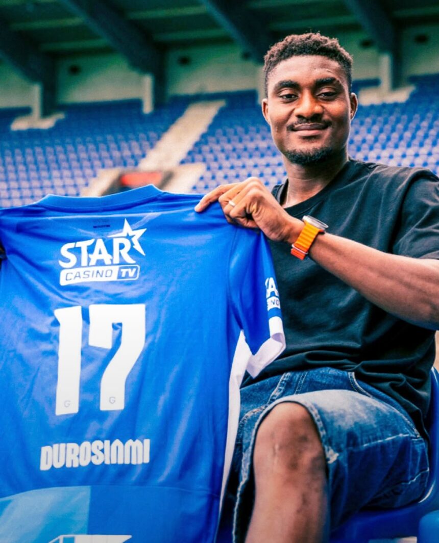 Smiling man in a black T shirt sits in a stadium holding up a blue sports jersey with the number 17 and logos STAR CASINO TV DUROSIMI  trybalnews