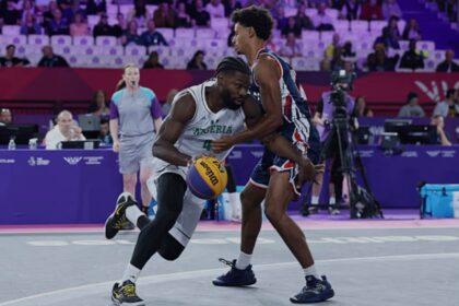 Basketball action: Nigeria player in white drives with the ball as a defender in blue/red guards him on a purple-court arena.