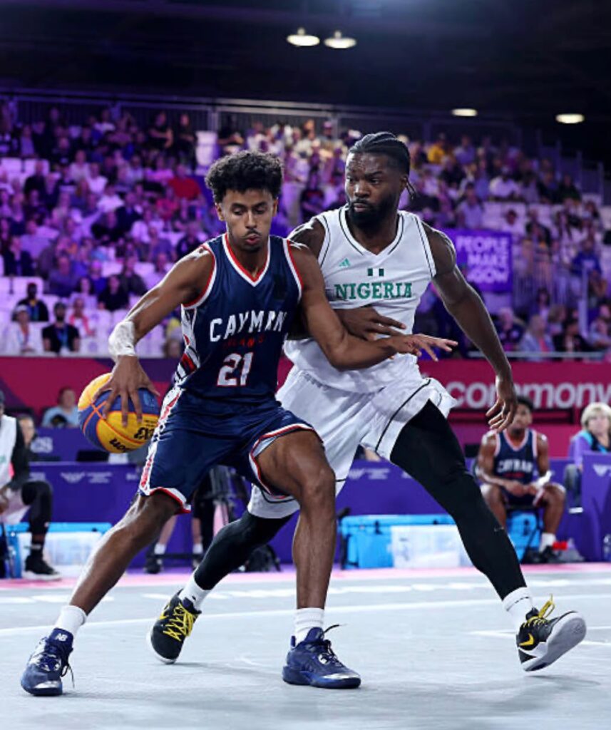 Glasgow Commonwealth Trybal News Two male basketball playersone in a dark Cayman jersey No 21 driving with the ball while a Nigerian defender in white guards him crowded arena in the background trybalnews