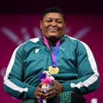 Smiling athlete in a teal tracksuit with a gold medal on a purple ribbon holding a small stuffed toy against a pink background  trybalnews