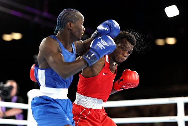 Glasgow Commonwealth Trybal News Two male boxers in a ring a blue uniform fighter landing a punch on a red uniform opponent as they trade blows trybalnews