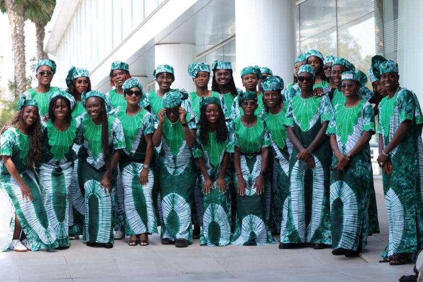Group of people in matching green and white traditional outfits posing outdoors in front of a modern glass building  trybalnews