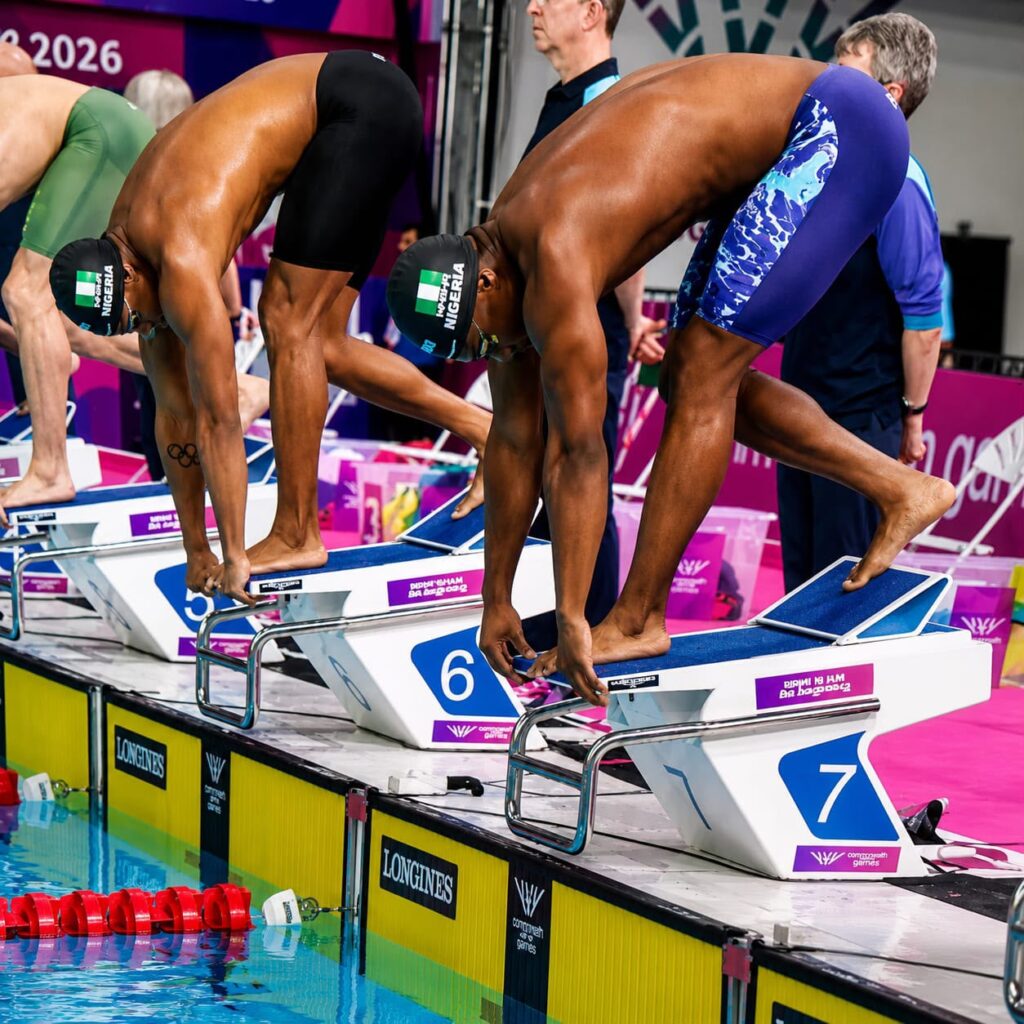 Swimmers in starting blocks at a colorful pool deck bent over and ready to dive wearing Nigeria caps  trybalnews