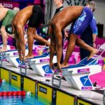 Swimmers in starting blocks at a colorful pool deck bent over and ready to dive wearing Nigeria caps  trybalnews