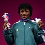 Young athlete in a teal PUMA jacket stands against a magenta background proudly holding a small trophy with a plush toy in one hand and medals in the other smiling at the camera  trybalnews