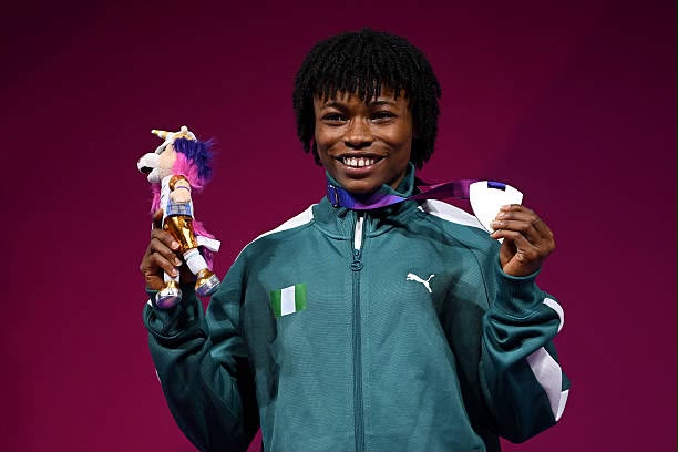 Young athlete in a teal PUMA jacket stands against a magenta background proudly holding a small trophy with a plush toy in one hand and medals in the other smiling at the camera  trybalnews