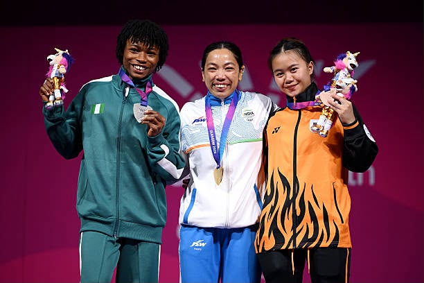 Three athletes stand on a podium with medals around their necks and small trophies smiling at the camera  trybalnews