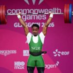 Nigerian weightlifter in green lifts a loaded barbell overhead at the Commonwealth Games stage 2016  trybalnews