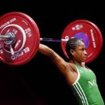 Female weightlifter in a green singlet lifts a barbell with red 25 kg plates labeled Glasgow 2016 against a black background  trybalnews