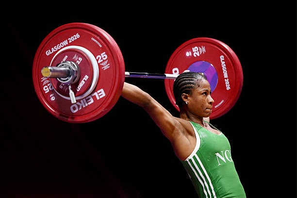 Female weightlifter in a green singlet lifts a barbell with red 25 kg plates labeled Glasgow 2016 against a black background  trybalnews