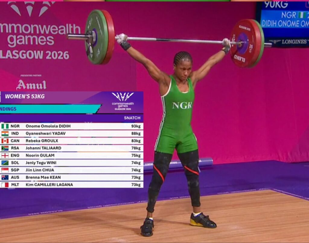 Glasgow 2026 Trybal News Weightlifter in a green singlet lifts a loaded barbell overhead during the Glasgow 2026 Commonwealth Games womens 53kg trybalnews