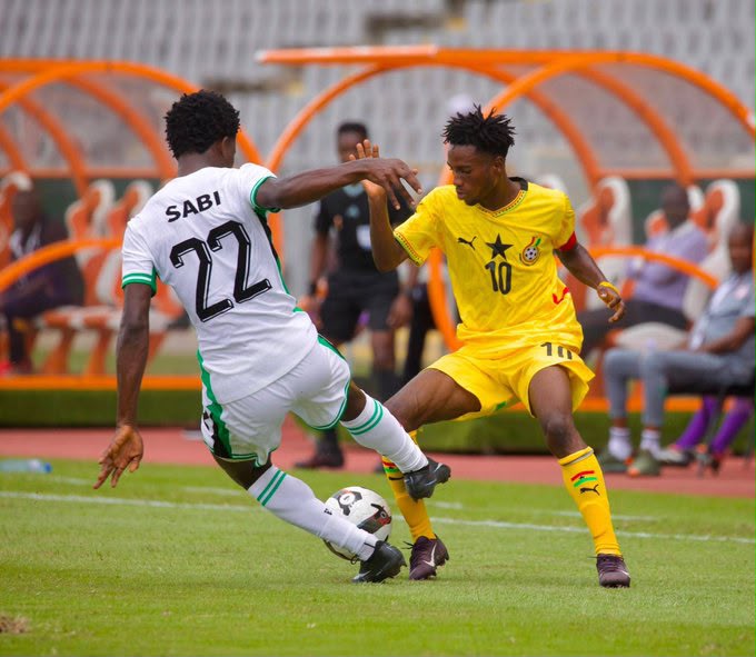 Two soccer players in white and yellow kits contest the ball on a grass field during a match with a teammate bench visible in the background  trybalnews
