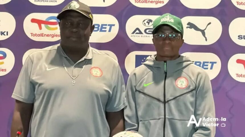 Two men pose for a photo at a sports event backdrop with sponsor logos both wear gray tops one with a cap and cross necklace the other in a green cap and zip jacket with a crest on the chest  trybalnews