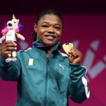 Female athlete on a podium smiling holding a gold medal in one hand and a plush unicorn trophy in the other wearing a teal jacket with an Irish flag patch  trybalnews