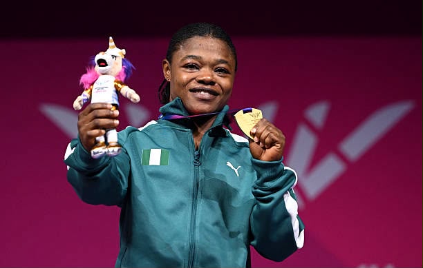 Female athlete on a podium smiling holding a gold medal in one hand and a plush unicorn trophy in the other wearing a teal jacket with an Irish flag patch  trybalnews