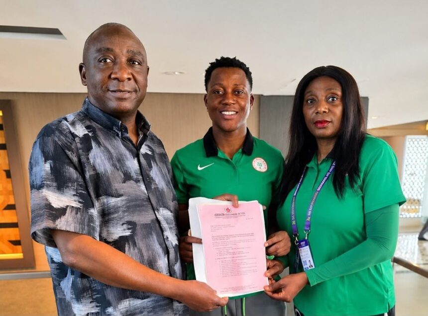 Three people stand indoors as they hand a pink certificate celebrating an achievement  trybalnews
