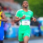 Two male sprinters race on a track foreground runner in green Nigeria kit with bib UDO LONGINES  trybalnews