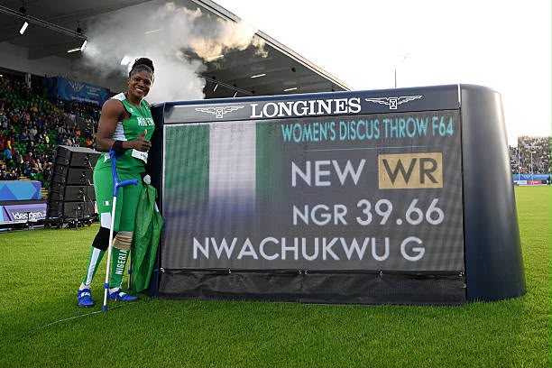 Female para athlete in a green uniform stands beside a stadium scoreboard announcing a new world record in womens discus throw F64 3966  trybalnews