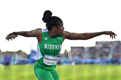 Female Nigerian track and field athlete in a green uniform throwing discus with arms extended mid-throw on a field.