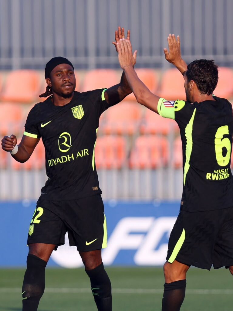 Two soccer players in black neon yellow kits high fiving on the pitch during a match Riyadh Air sponsor visible on front  trybalnews