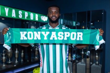 Footballer in green-and-white striped jersey holds a Konya Spor scarf in front of a trophy-filled room