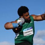 Male track and field athlete in a green uniform mid throw bib ENEKWECHI LONGINES against a blue sky background  trybalnews