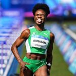 Female sprinter in a bright green uniform celebrating at a track event tongue out bib reads AMUSAN  trybalnews