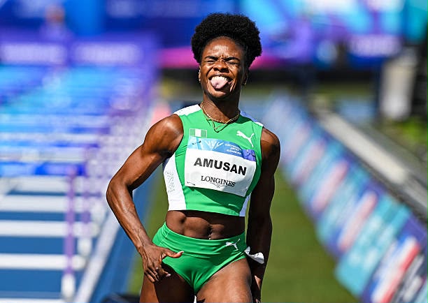 Female sprinter in a bright green uniform celebrating at a track event tongue out bib reads AMUSAN  trybalnews