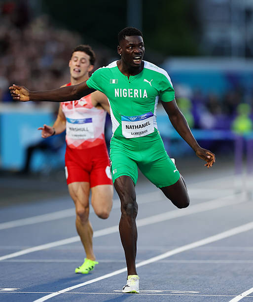 Glasgow 2026 Trybal News Nigerian sprinter in green crosses the finish line on a blue track arms outstretched as a rival in red finishes behind him trybalnews