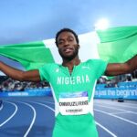 Nigerian sprinter on the track celebrates with a green Nigerian flag raised behind him crowded stadium in the background  trybalnews