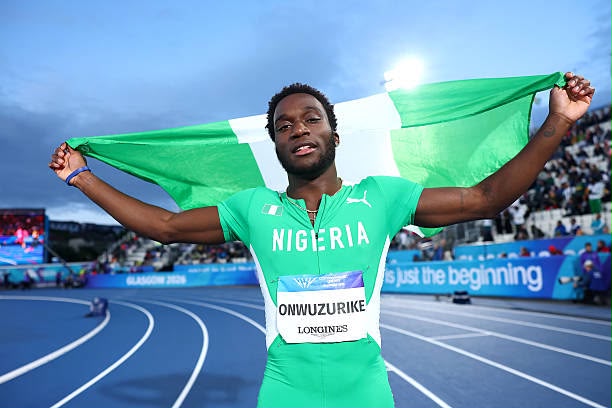 Nigerian sprinter on the track celebrates with a green Nigerian flag raised behind him crowded stadium in the background  trybalnews