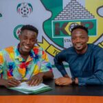 Zayyad Musa wearing a colorful multi colored shirt signs his contract at a table while seated next to Kano Pillars Club Ambassador Ahmed Musa in a blue traditional outfit Both are smiling The Kano Pillars crest and NPFL logos are visible on the backdrop Photo Credit Kano Pillars  trybalnews
