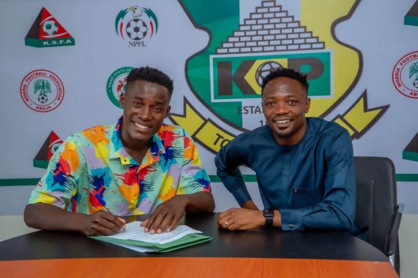Zayyad Musa wearing a colorful multi colored shirt signs his contract at a table while seated next to Kano Pillars Club Ambassador Ahmed Musa in a blue traditional outfit Both are smiling The Kano Pillars crest and NPFL logos are visible on the backdrop Photo Credit Kano Pillars  trybalnews