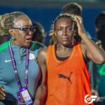 Female athlete in an orange jersey looks distressed as a coach with braided hair consoles her after a race in a sports venue Informative  trybalnews